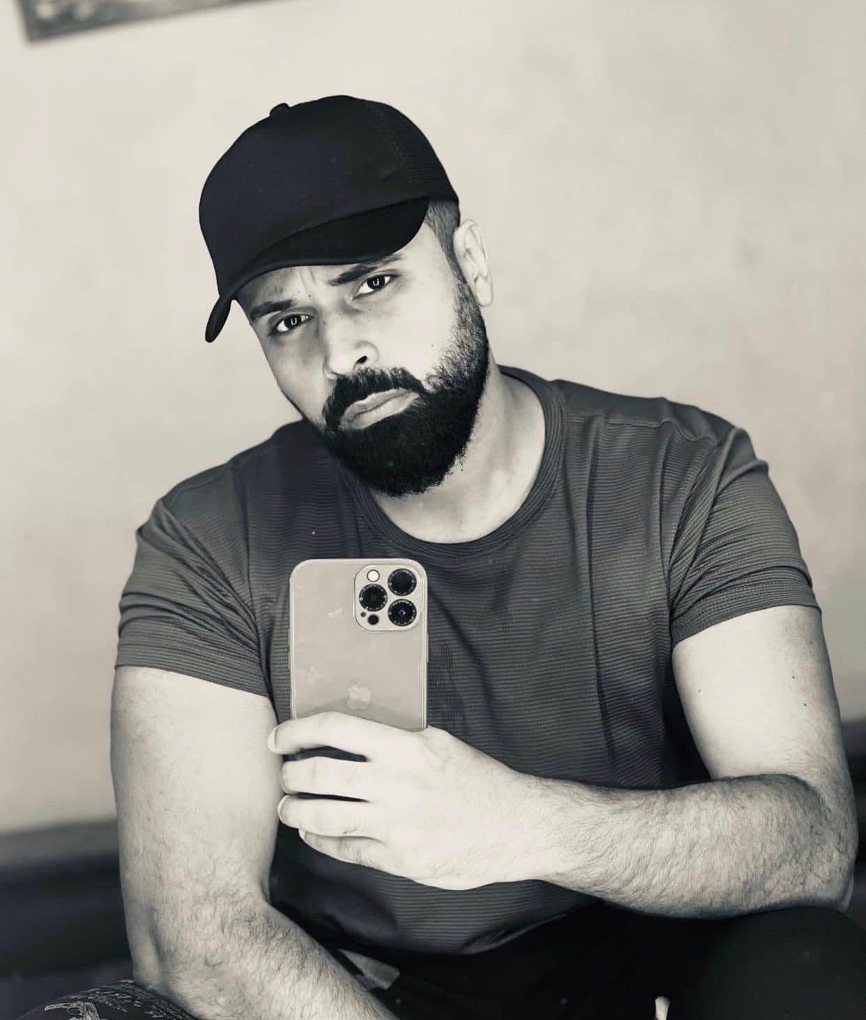 Un homme barbu avec une casquette noire prend un selfie en noir et blanc.